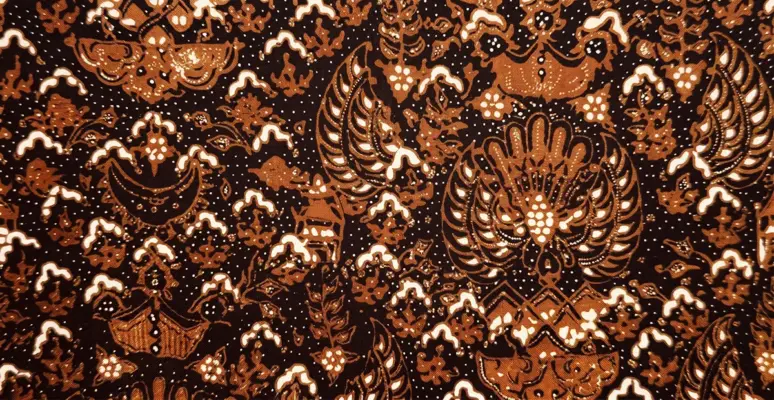 Close-up of authentic Batik Cuwiri fabric featuring Sogan brown Meru mountain and Garuda wing motifs with white cecek dots on a hand-dyed black cotton background